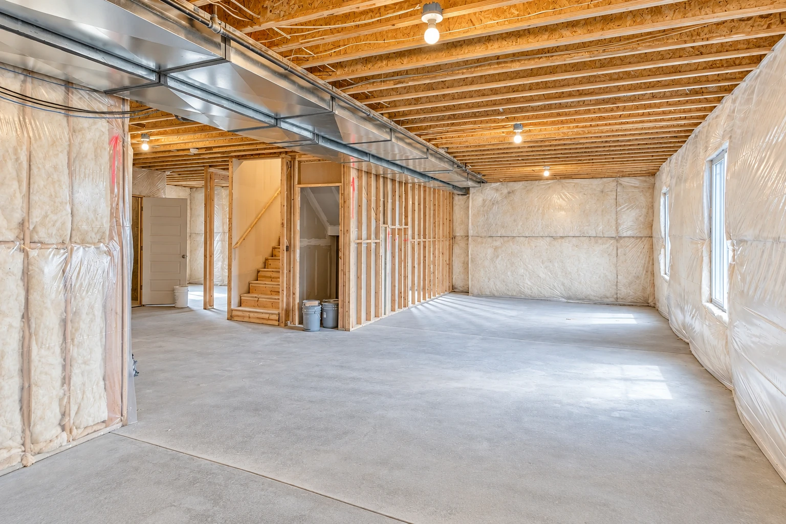 Unfinished basement with insulation batts covering the walls, exposed ceiling joists, and a metal air duct.