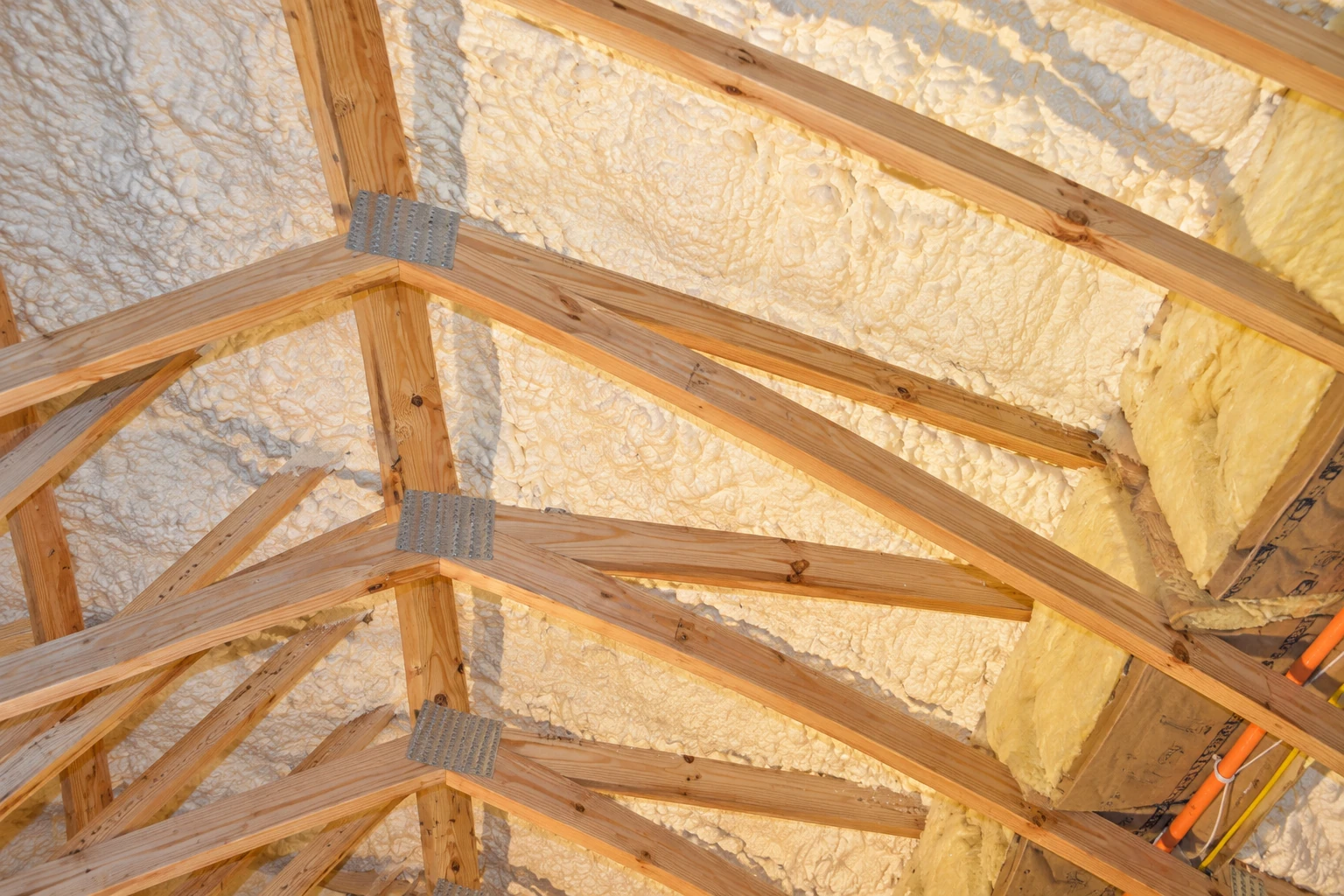 Closed-cell foam insulation coats the underside of a roof between exposed wooden rafters.